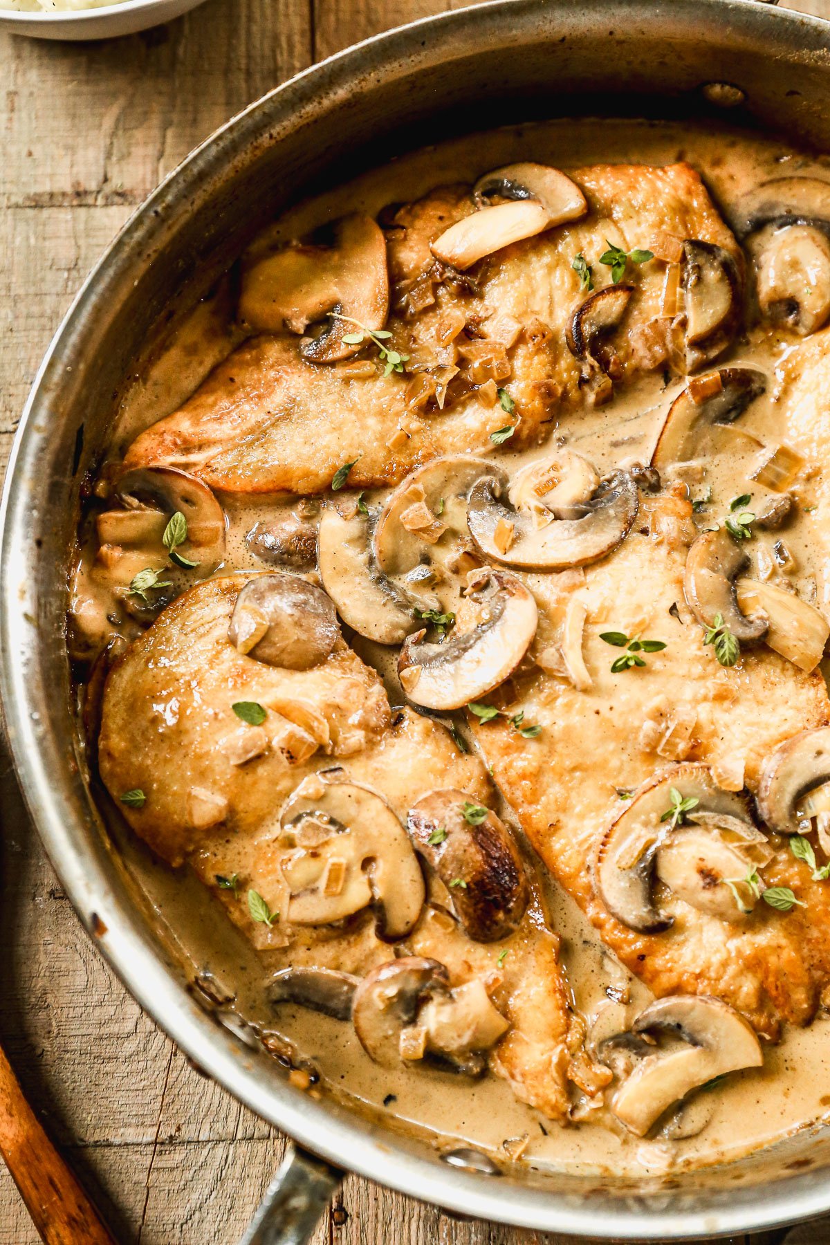 Mushroom chicken in a creamy sauce, garnished with fresh herbs, cooked in a skillet on a wooden surface.