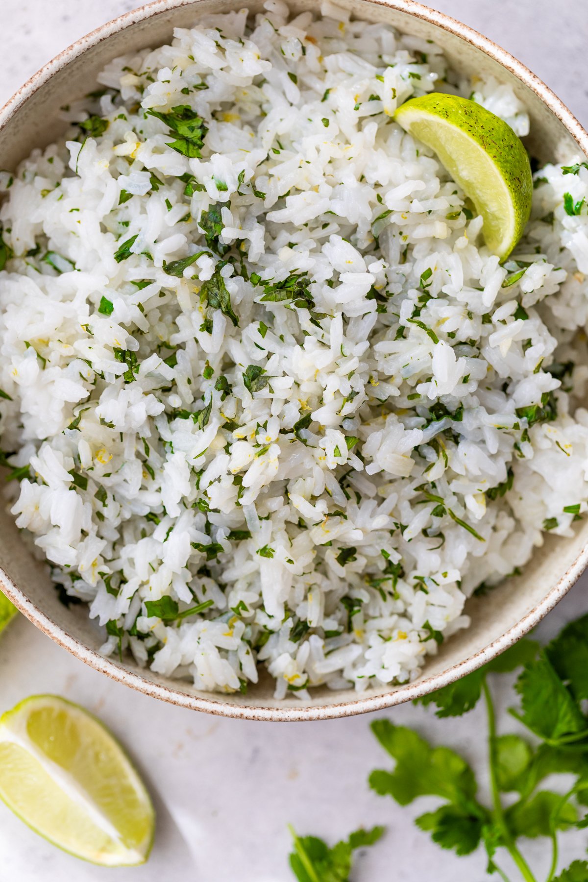 A bowl of cilantro lime rice, garnished with a wedge of lime. Extra lime wedges and fresh cilantro are on the table nearby.