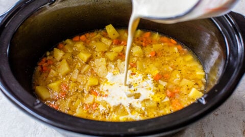 milk being poured over potatoes in a slow cooker for potato soup