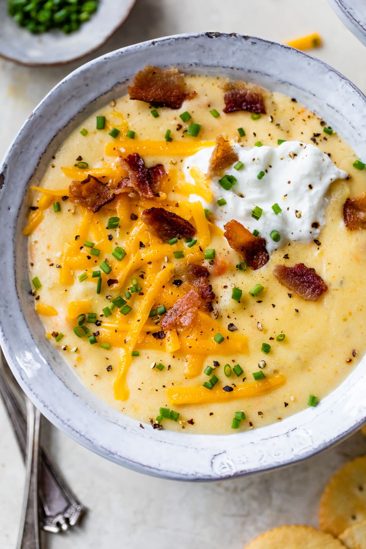 bacon, cheese, and greek yogurt on top of healthy Crockpot Potato Soup with evaporated milk in a bowl