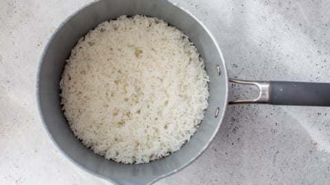 A pot filled with freshly cooked white rice sits on a light gray textured surface, viewed from above.