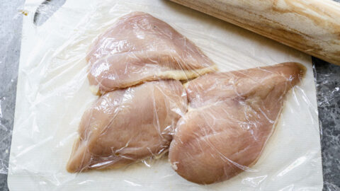 Three raw chicken breasts under plastic wrap