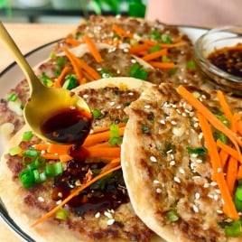 A hand drizzles dark soy sauce over crispy smashed dumpling tacos